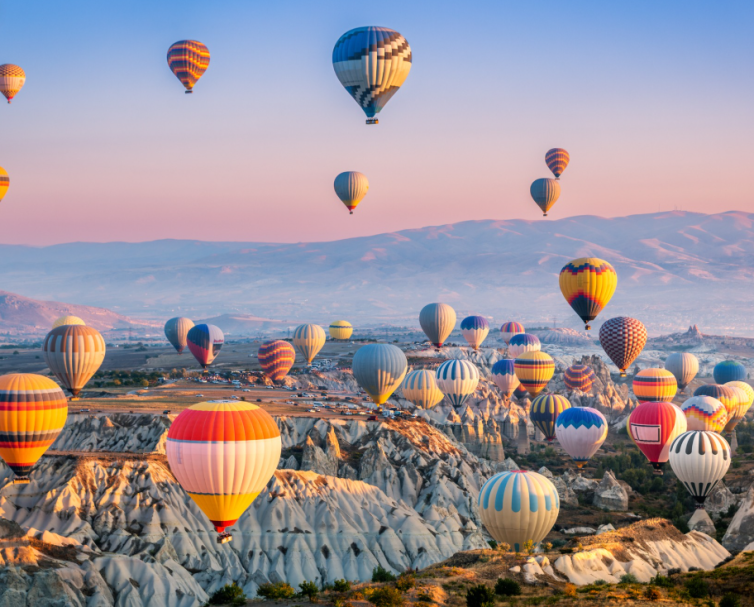 Colourful hot air balloons soaring over a scenic landscape at sunrise.
